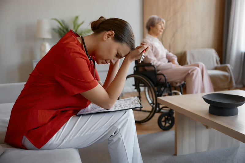 Exhausted caregiver sitting beside an older adult in a wheelchair, representing caregiver burnout and stress.